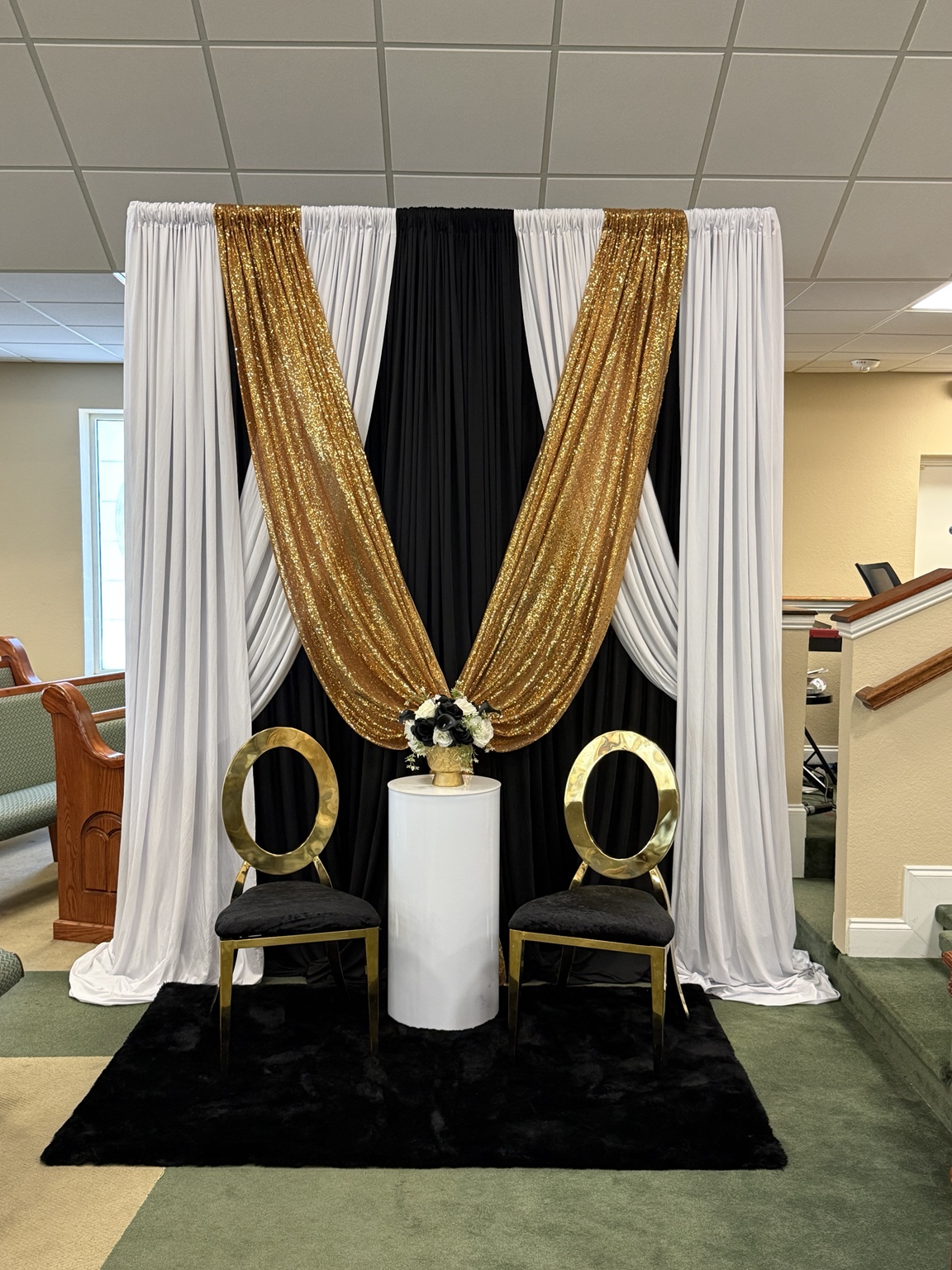 White, gold, and black draping around a two-chair event setup